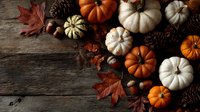 Autumn harvest display with white and orange pumpkins, pine cones, acorns, and maple leaves arranged on rustic wooden background.