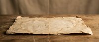 Ancient weathered parchment scroll with torn edges on rustic wooden surface, vintage manuscript paper for historical documents and antique designs.
