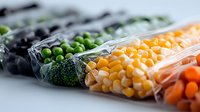 Frozen mixed vegetables in transparent plastic bags arranged in row showing peas, corn, broccoli and carrots, fresh produce preservation concept.