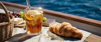 Iced tea and croissant on a sunny boat deck with ocean view, perfect for travel, leisure, and food lifestyle content.