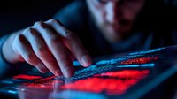 Hacker typing on illuminated keyboard with red and blue light in dark room, dramatic cybersecurity concept showing digital threat and online crime.