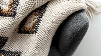 Macro view of white knitted winter glove with traditional Nordic pattern and black leather palm detail showing texture and craftsmanship in cold weather accessories.