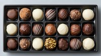 Luxury chocolate truffles and pralines assortment in elegant black box with dark, milk, and white chocolate varieties, decorated with nuts and stripes.
