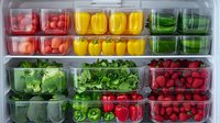 Fresh produce organized in clear containers showing meal prep with colorful bell peppers, leafy greens, radishes, and berries arranged in refrigerator compartments.