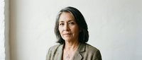 Professional mature Hispanic businesswoman in beige blazer standing confidently in modern office environment for corporate leadership presentations.