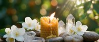 Spa wellness scene with burning candle, white jasmine flowers, healing crystals and smooth stones on natural background with soft bokeh lighting.