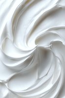 Swirling white cream texture with soft peaks and valleys creating an elegant abstract pattern, suitable for cosmetic, food, or beauty product advertising backgrounds.