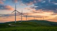 Wind turbines on green hills at sunset with dramatic colorful sky and winding path for renewable energy and sustainability concepts.