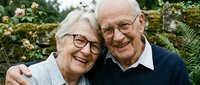 Happy elderly Caucasian couple embracing and laughing together in garden setting. Senior man and woman with glasses showing joy and love in retirement years.