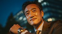Confident Asian businessman in suit smiling outdoors at dusk with city lights background for corporate marketing and professional success concepts.
