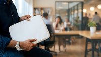 Man holding blank white tablet in modern office with colleagues working in background, suitable for business communication and corporate messaging concepts.
