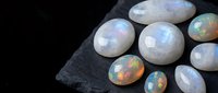Collection of natural rainbow opal gemstones displaying iridescent fire colors on dark slate surface for jewelry making and mineral specimens.