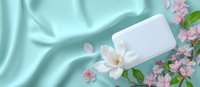 Elegant white blank card with magnolia flower on mint green silk fabric background with pink spring blossoms, romantic floral composition.