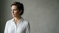 Professional middle-aged Caucasian businesswoman in white shirt looking thoughtfully to side against neutral gray background for corporate presentations.