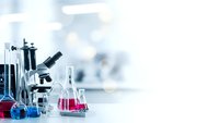 Laboratory equipment with microscope and colorful chemical solutions in glassware on white table for scientific research and medical testing.