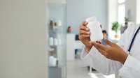 Closeup of healthcare professional holding blank white bottle for skincare, cosmetics, or medical product packaging in modern clinic setting.