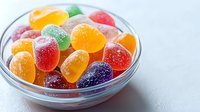 Colorful sugar coated jelly candies in glass bowl on light background. Sweet fruit gummy drops with crystal sugar coating for confectionery and dessert designs.