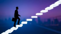 Young male professional of South Asian descent in business attire climbing illuminated ascending staircase against purple twilight cityscape, symbolizing career growth, ambition, and success in corporate advancement.