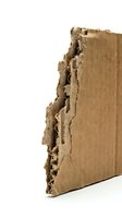 Torn and damaged corrugated cardboard edge with exposed wavy layers against white background, suitable for packaging, recycling, and shipping concepts.