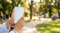 Hands holding reusable water pouch outdoors in sunny park setting, promoting eco-friendly hydration and sustainable lifestyle choices for beverage packaging.
