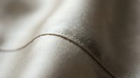 Close-up macro shot of beige leather texture with visible stitching and natural grain patterns. Soft lighting highlights material quality and craftsmanship details.