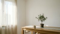 Minimalist dining room interior with wooden table, small potted plant and white mug. Natural light through sheer curtains creates peaceful atmosphere for home decor.