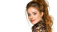 Young Caucasian woman with ginger hair and natural makeup wearing brown leopard print coat smiling at camera against white background. Isolated portrait for fashion and beauty content.