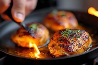 Juicy chicken thighs with crispy skin searing in cast iron pan with flames and caramelized glaze, garnished with fresh herbs for gourmet cooking.