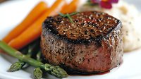 Juicy grilled beef tenderloin steak with black pepper crust, served with fresh asparagus spears, baby carrots and mashed potatoes on white plate.