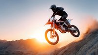 Motocross rider jumping dirt bike against dramatic sunset sky with mountain silhouette, extreme sports action shot for adventure and adrenaline concepts.