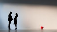 Silhouette of couple holding hands with red heart shape on floor, romantic minimalist scene against light gradient background. Love story concept.