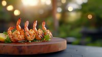 Grilled shrimp skewers on wooden serving board with herbs and seasonings against blurred garden background with bokeh lights.