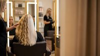 Blonde woman getting hair styled at professional salon with stylist working in modern beauty parlor with illuminated mirrors for hair care services.