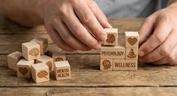 Hands arranging wooden blocks with mental health and wellness symbols on rustic table for therapy and psychological wellbeing concepts.
