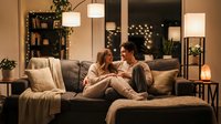 Cozy couple relaxing together on sofa in warm modern living room with soft lighting and comfortable home decor creating intimate romantic atmosphere.