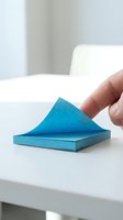 Hand peeling blue adhesive note from white surface, isolated on clean background. Sticky memo pad ready for design use.