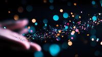 Glowing particles and bokeh lights stream across dark background in vibrant cyan, pink, and gold tones, creating dynamic motion effect for digital design projects.