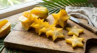 Fresh yellow star fruit slices on wooden cutting board with knife, tropical exotic carambola ready for healthy snacking and culinary preparation.