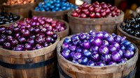 Colorful chocolate candy balls in wooden baskets at market display. Shiny foil wrapped confectionery in purple, blue, and pink metallic packaging creates festive arrangement.