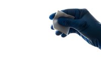 Medical professional hand in blue latex glove holding white pill or medication tablet against clean white background for healthcare design.