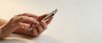Female hands holding smartphone on light textured surface for communication and technology concepts in modern lifestyle applications.
