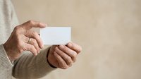 Senior man with weathered hands holding blank white card against neutral background, suitable for business cards, invitations, promotional materials, and corporate messaging.
