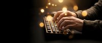 Hands typing on laptop keyboard with warm golden bokeh lights creating atmospheric glow for technology and digital work concepts.