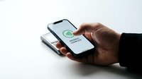 African American businessman hand holding smartphone with contactless payment complete confirmation screen over wireless charging pad for mobile commerce transaction.