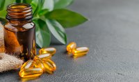 Omega-3 fish oil capsules with brown glass bottle and green leaves on gray concrete background, natural supplements and vitamins for health benefits.