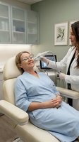 Female dermatologist performing laser skin treatment on mature Caucasian woman patient in modern medical clinic with advanced cosmetic equipment.