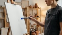 Young male artist painting on blank canvas with brush in art studio workspace with easel and supplies for creative expression and artistic development.