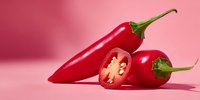 Fresh red chili peppers with green stems on pink background, one sliced showing seeds and interior, spicy cooking ingredient for culinary recipes and food preparation.