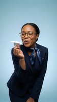 Professional African American businesswoman in navy suit holding paper airplane with playful expression and glasses on blue background.