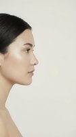 Young woman profile portrait with natural makeup and slicked back hair on neutral background for beauty and skincare concepts.